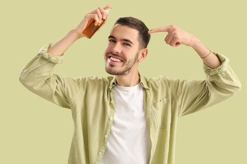 Young man pointing at product for hair growth on green background