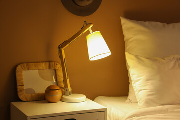 Glowing lamp with frame on table in dark bedroom at night