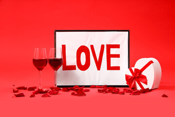 Painting with word LOVE, glasses of wine and gift on red background. Valentine's Day celebration