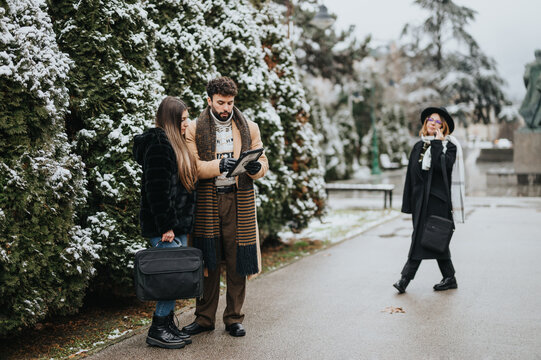 A couple examines a map together, holding luggage in a snowy park, while a cheerful woman walks by, carrying a suitcase and smiling.