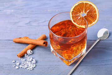 Glass of delicious Old Fashioned Cocktail with orange slice and cinnamon sticks on purple wooden...