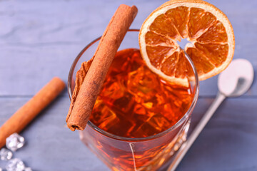 Glass of delicious Old Fashioned Cocktail with orange slice and cinnamon sticks on purple wooden...