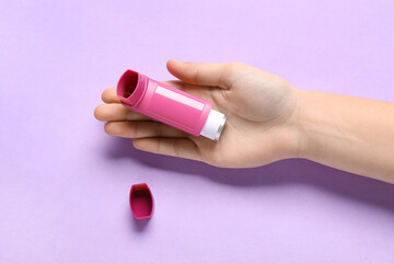Child's hand with asthma inhaler on lilac background