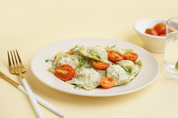 Plate of tasty ravioli with tomatoes and cheese on yellow background