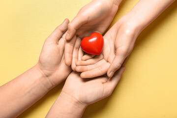 Hands of woman and child holding red heart on yellow background