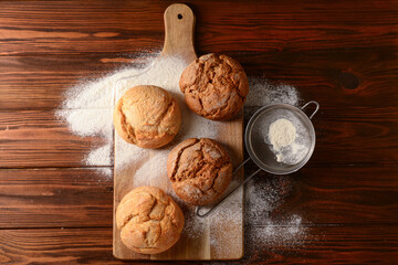 Fototapeta na wymiar Board with fresh delicious buns and flour on wooden background