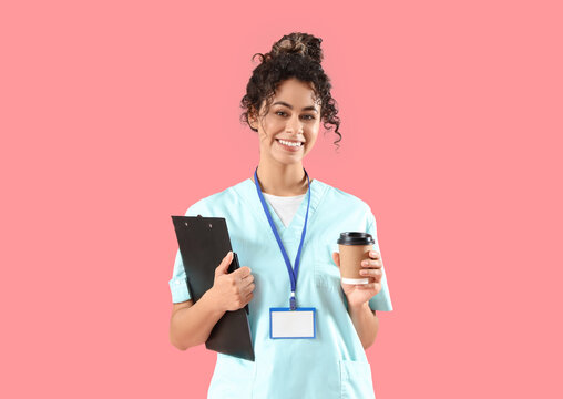 Female African-American medical intern with clipboard and coffee cup on pink background