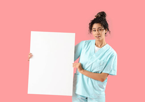 Female African-American medical intern with blank poster on pink background