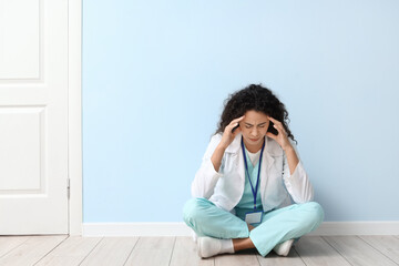 stressed female African-American medical intern sitting near blue wall