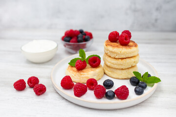 Cottage cheese pancake or syrniki with fresh raspberries and blueberry on white wooden table.  Sweet breakfast or lunch, tasty dessert. 