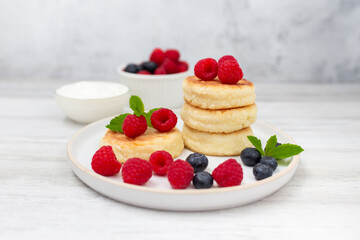 Cottage cheese pancake or syrniki with fresh raspberries and blueberry on white wooden table.  Sweet breakfast or lunch, tasty dessert. 
