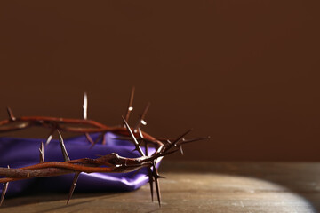 Crown of thorns with purple fabric on wooden table against brown background