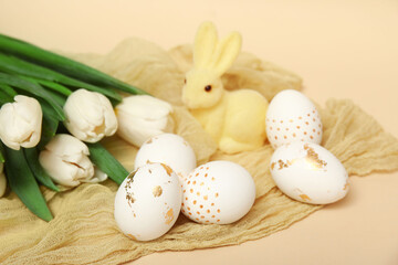 Easter eggs with tulips and bunny figurine on beige background