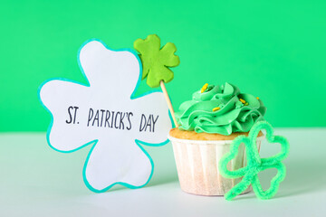 Tasty cupcake with clovers and festive postcard for St. Patrick's Day on white table against green...