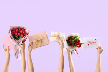 Female hands with bouquets of tulips, festive postcard and gift boxes on lilac background. Shopping...