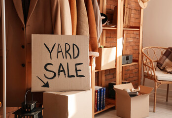 Cardboard with text YARD SALE and various unwanted things near brick wall in room