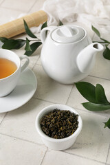 Teapot and bowl with dry leaves on white tile background, closeup