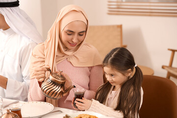 Happy Muslim mother pouring tea for her little daughter at family dinner. Ramadan celebration