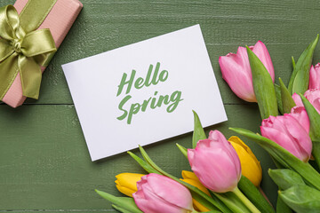 Greeting card with text HELLO SPRING, gift box and beautiful tulips on green wooden background