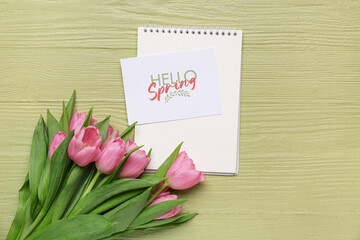 Greeting card with text HELLO SPRING, notebook and beautiful pink tulips on green wooden background