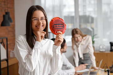 Businesswoman with whoopee cushion showing silence gesture in office. April Fools' Day celebration