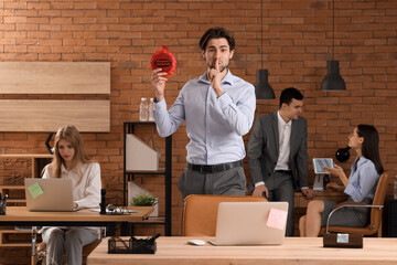 Business man with whoopee cushion showing silence gesture in office. April Fools' Day celebration
