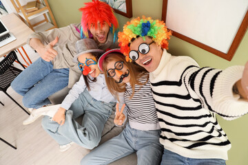 Young colleagues with funny disguise taking selfie in office. April Fools' Day celebration