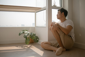 Sad and lonely Asian man sits on the floor hugging his knee.