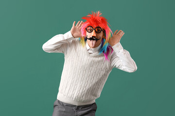 Businessman in funny disguise showing tongue on green background. April Fools' Day celebration