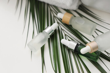 Cosmetic dropper bottles with palm leaf on white table, closeup