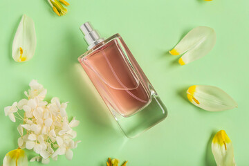 Pink bottle of perfume with petals and flowers on green background. Top view