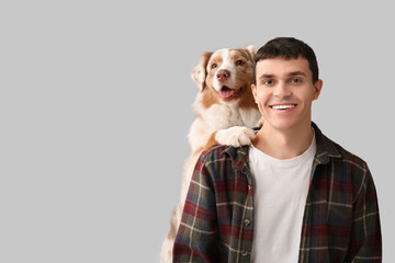 Young man with Australian Shepherd dog hugging on light background