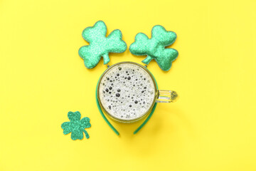 Glass of beer with headband and clover on yellow background. St. Patrick's Day celebration