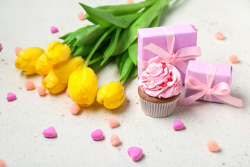 Presents, yellow tulips and tasty cupcake on light background
