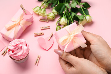 Female hands with beautiful gift box and cupcake on pink background