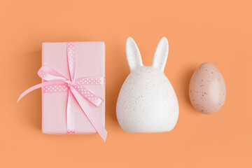 Easter gift, bunny figure and painted egg on orange background