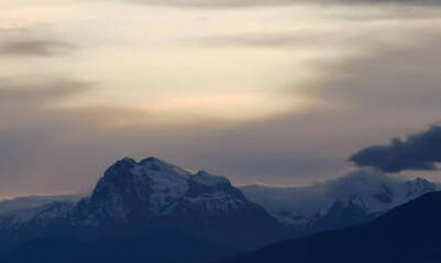 Le cime delle montagne innevate al tramonto nel cielo plumbeo invernale
