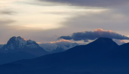 Le cime delle montagne innevate al tramonto nel cielo plumbeo invernale e nuvole bordate di rosso...