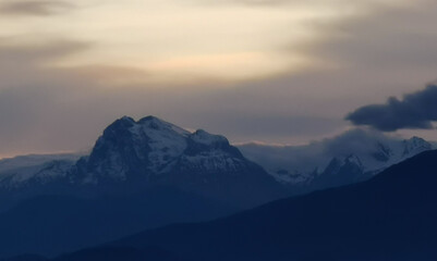 Obraz premium Le cime delle montagne innevate al tramonto nel cielo plumbeo invernale