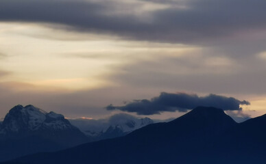 Fototapeta na wymiar Le cime delle montagne innevate al tramonto nel cielo plumbeo invernale