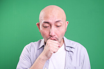 Asian bald man coughing into his fist on green background