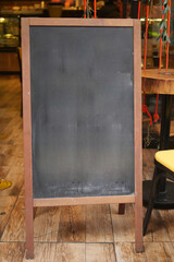 Empty wooden blackboard mockup standing outdoors in front of cafe 