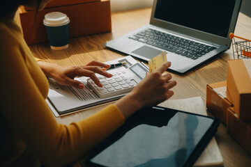 Young woman holding a smartphone, tablet showing payment success and credit card with yellow parcel...