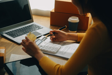 Young woman holding a smartphone, tablet showing payment success and credit card with yellow parcel box as online shopping concept in office