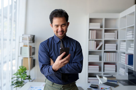 Businessman relaxes holding smartphone, checking email, work details on laptop computer online, contacting, business negotiation with customer pointing to successful business goals in office.