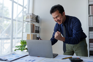 Businessman holding smartphone showing happy expression while receiving confirmation email on laptop Response to investment in financial business Earn bonuses based on successful business goals.