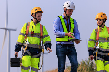 Engineers and inspector team wearing uniforms and helmets with equipment walking exploring and repairing electric wind turbines which are renewable energy for communities and agriculture.