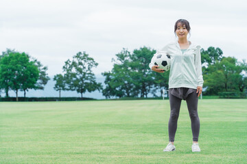運動場でサッカーボールを持つサッカーファン・サポーターの日本人女性
