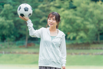 運動場でサッカーボールを持つサッカーファン・サポーターの日本人女性
