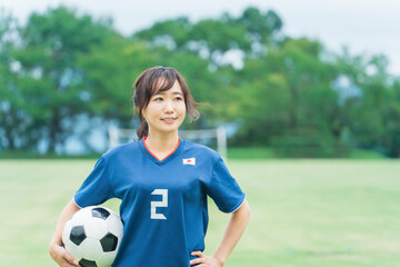 サッカーボールを持ちながら笑顔でサッカーするファン・サポーターの日本人女性
